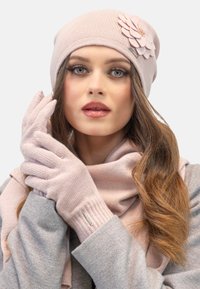 Berretto di lana rosa con un accento floreale, guanti abbinati di un rosa chiaro e una sciarpa morbida rosa. Materiale testurizzato con una finitura liscia.