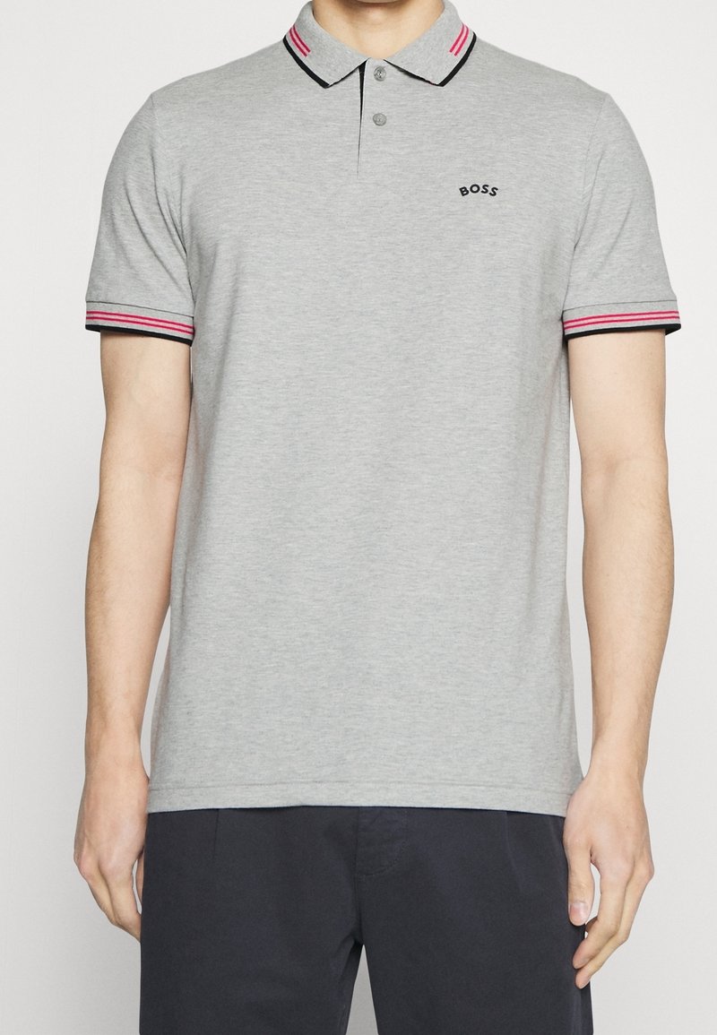 Grå polo t-shirt med korta ärmar, randiga röda och svarta detaljer på kragen och ärmarna, samt en logotyp på bröstet. Mjukt tyg.