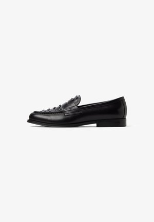 Loafer en cuir noir avec un bout rond, un design texturé et des clous décoratifs sur le dessus. Il présente un petit talon et une silhouette élégante.
