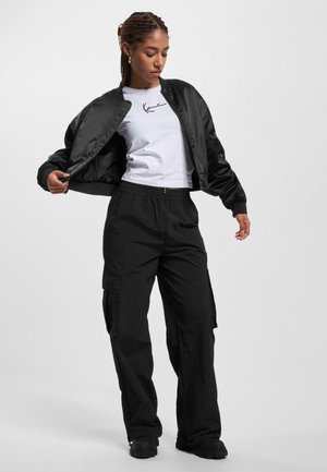 Jacket bomber negru peste un tricou alb cu grafică neagră, asortat cu pantaloni cargo negri, largi. Material neted, ajustare relaxată.