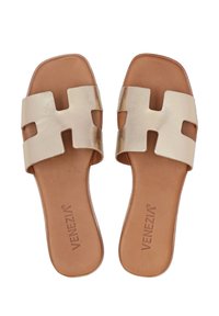 Gouden metalen slide-sandalen met een brede uitgesneden band, tan lederen voetbed, platte zool en gegraveerd merkteken op de binnenzool.