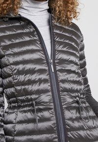 Graue Pufferjacke mit ge quiltetem Design, Reißverschluss vorne und verstellbaren Kordeln in der Taille. Hergestellt aus glänzendem, glattem Stoff.