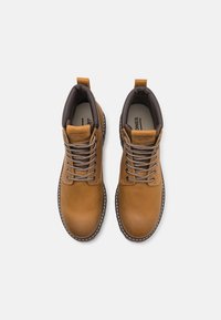 Botas de cuero marrón hasta el tobillo con acentos grises, que cuentan con cordones redondos, un cuello acolchado y una suela texturizada. Detalles de costura a lo largo de los bordes.