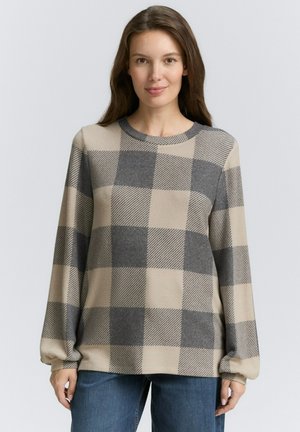 Beige long-sleeve sweater featuring a large grey checkered pattern, round neckline, and ribbed cuffs, paired with blue denim jeans.