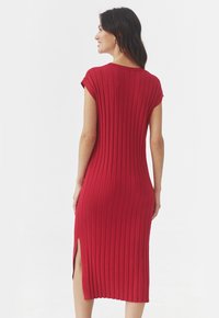 Punane ribadega midi kleit lühikeste varrukatega, külgslitside ja kitseneva silueti kirjeldus, mis annab elegantse välimuse. Pehme kudumitekstuur.
