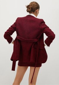 Bordowy blazer o fakturze z paskiem w talii, z podwójnymi kieszeniami, luźnym krojem i klasycznym kołnierzykiem, prezentujący lekko oversize'owy design.