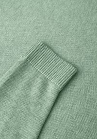 Jasnozielona dzianina z ryflem, charakteryzująca się gładką fakturą i równomiernym, jednolitym ściegiem przez całą powierzchnię.