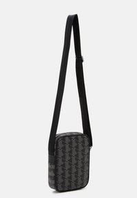 Black crossbody bag with geometric pattern, smooth texture, adjustable strap, and zip closure, featuring silver hardware accents.