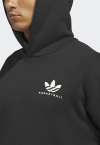 Close-up of a person wearing a black hoodie with a white Adidas trefoil logo and "BASKETBALL" text on the chest.