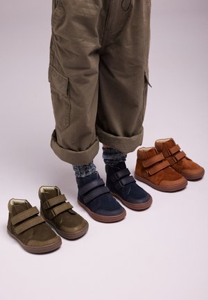 Cuatro pares de zapatos infantiles: verde oliva, azul marino y marrón óxido. Cada uno tiene un diseño de caña alta con correas de Velcro y suelas de goma.