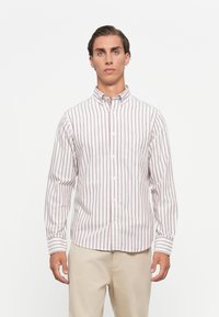 Striped button-up shirt in white with red vertical stripes, featuring a collar and single chest pocket. Made of lightweight cotton fabric.