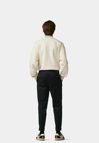 Crème sweatshirt, zwarte tapered broek en sneakers met een patroon en een gele accent. Casual outfit gezien van de achterkant, minimalistische achtergrond.
