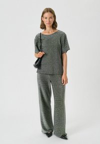 Glitzerndes graues Strickoberteil und passende weite Hose, Rundhalsausschnitt, kurze Ärmel und weiche Textur, ergänzt durch schwarze Accessoires.