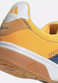 Baskets Adidas jaunes en tissu mesh, avec un patch en daim marron au talon, une semelle blanche et le logo Adidas embossé sur la semelle en caoutchouc.