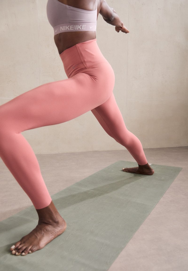 Leggings rosa de cintura alta y un sujetador deportivo lila claro, sobre una esterilla de yoga verde en un suelo gris texturizado.