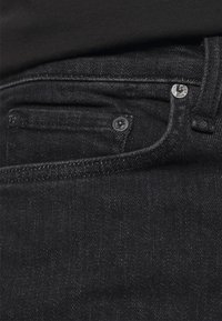Jeans de mezclilla negra con una textura suave, que cuentan con un bolsillo para monedas, botones de metal y detalles de costura sutiles a lo largo de los bolsillos y la cinturilla.