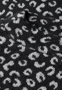 Tessuto a maglia nera con motivo leopardato irregolare bianco, che mostra la texture e le pieghe.