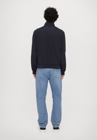 Chaqueta de bombardero navy con cuello alto, puños y dobladillo elásticos, combinada con vaqueros de corte holgado en azul claro y zapatillas negras.