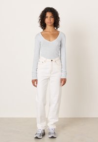 Dugi sivim rukavima, V-izrez na vrhu u kombinaciji s bijelim trapericama visokog struka. Model nosi sive i bijele tenisice. Mekana tekstura i ležerni kroj.