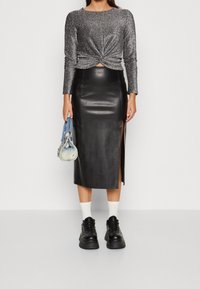 Skimrande grå långärmad topp med knut framtill, ihopparad med en högmidjad svart läderkjol med sidoklipp, och kraftiga svarta sneakers.