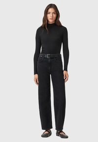Top nero a maniche lunghe, jeans neri a vita alta, cintura con borchie e scarpe slip-on nere con accenti bianchi. Design semplice e contemporaneo.