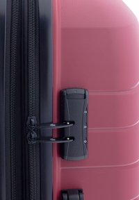 Valigia rigida rossa con superficie testurizzata, cerniere nere e meccanismo a doppia serratura. Presenta bordi lisci e arrotondati e un design elegante.