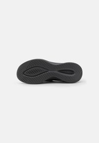 Suela de zapato deportivo negro con una superficie de goma texturizada, que presenta un patrón ondulado y ranuras laterales para tracción y flexibilidad.
