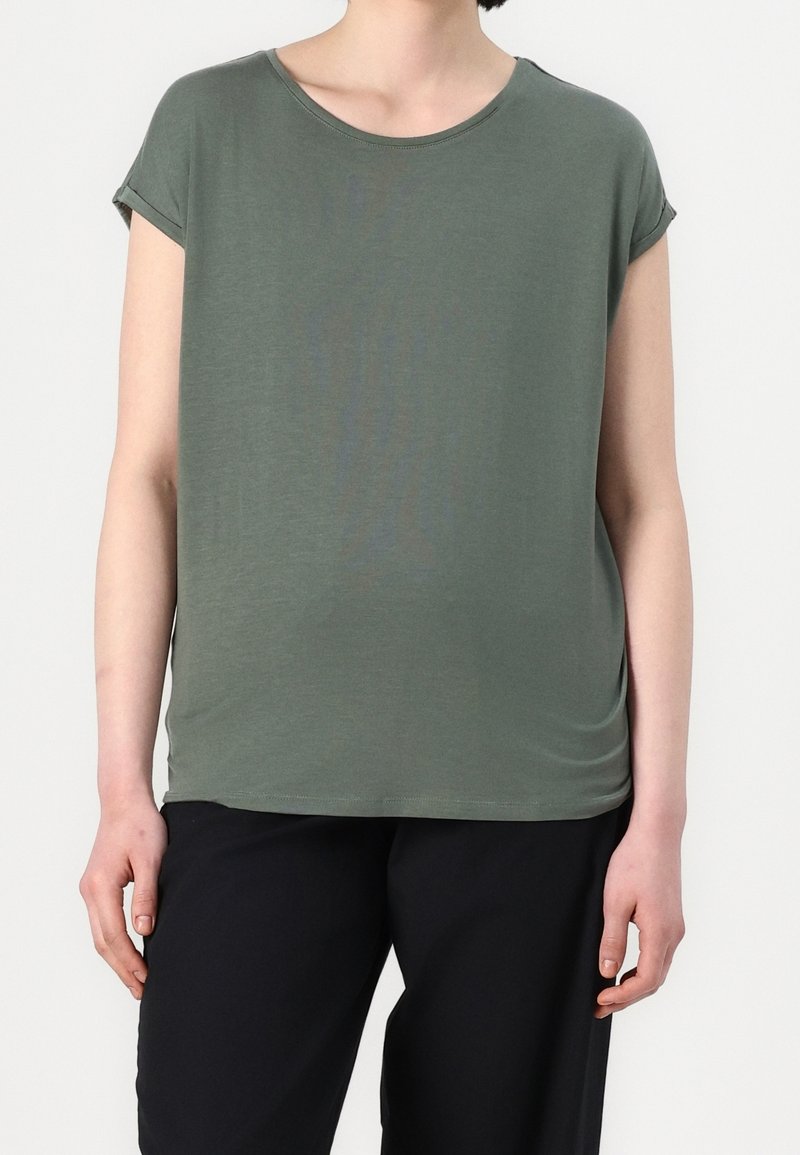 T-shirt à manches courtes vert olive avec un col rond, une texture douce, une coupe décontractée et des poignets retroussés, associé à un pantalon noir ample.