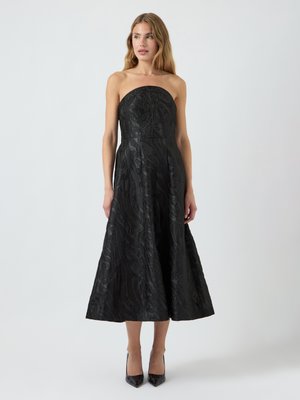 Vestido negro sin tirantes con un torso ajustado y una falda acampanada. La tela texturizada presenta un patrón de hojas. Un par de tacones altos negros.