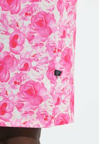 Primer plano de una falda con un patrón floral de color rosa brillante y una pequeña etiqueta de tela negra en el lateral.