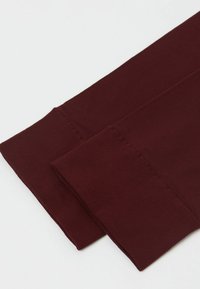 Bordové legíny s texturovaným, žebrovaným lemem. Materiál je elastický, hladký a přiléhavý, s odolným šitím podél okrajů.