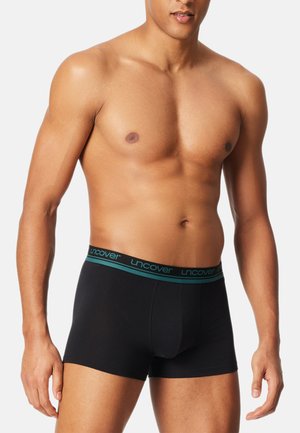 Schwarze Boxershorts aus weichem Stoff, mit einem türkisfarbenen elastischen Bund, auf dem der Markenname "uncover" steht. Figurbetontes Design ohne Muster.