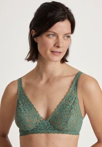 Lace bralette in gedempt groen met een driehoekige vorm, scalloped randen en een bloemenpatroon. Zachte textuur en verstelbare schouderbanden.