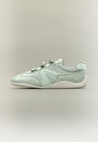 Baskets en daim vert clair avec des lacets assortis, une semelle blanche et des détails incurvés sur le côté, présentées de profil sur un fond neutre.