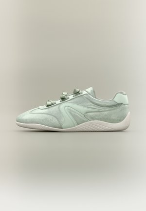 Baskets en daim vert clair avec des lacets assortis, une semelle blanche et des détails incurvés sur le côté, présentées de profil sur un fond neutre.