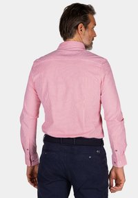 Rood-witte gestreepte lange mouwen shirt met knoopmanchetten, met een effen achterkant, gecombineerd met donkere broek en een geweven zwarte riem.