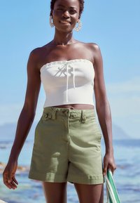 Un short vert à taille haute, avec une fermeture à bouton et des poches latérales, associé à un top blanc sans bretelles avec un cordon de serrage.