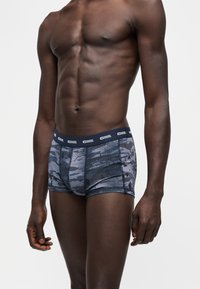 Mannequin masculin portant un boxer Diesel bleu à motif camouflage avec une ceinture élastique siglée, présenté du torse au milieu des cuisses sur un fond uni.