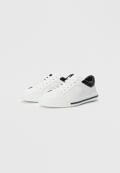 Pair of white low-top sneakers with white laces, black heel collar, and black stripe detail on white rubber soles.