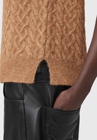 Brun strikket sweater med kabelmønster og en vinkelret udsparing i kanten, parret med sorte læderbukser med en sidelomme.