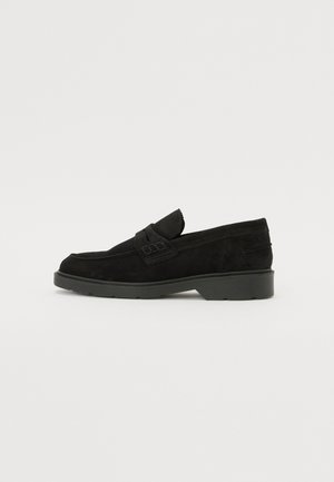 Mocassins en cuir suédé noir à talon bas, avec une band simple sur le dessus et des détails texturés le long des côtés.
