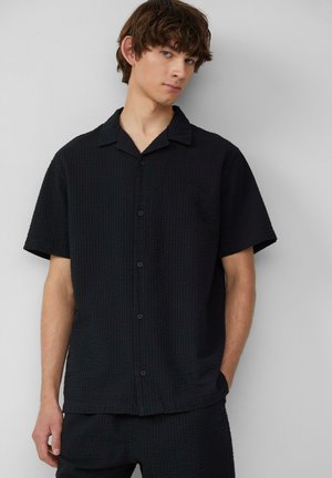 Czarna krótkosleeve'owa koszula zapinana na guziki z teksturowanym, waflowym wzorem, z wykładanym kołnierzykiem i zapięciem na guziki z przodu. Poziome szwy na dole.