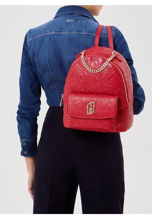 Červený texturovaný batoh z umělé kůže, vybavený přední kapsou, zlatým řetízkovým akcentem a zapínáním na zip. Nositelný na zádech.