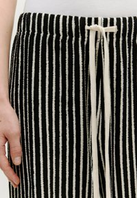 Zwart-wit gestreepte stof met een textuurafwerking. Voorzien van een trekkoord in de taille en een recht model.