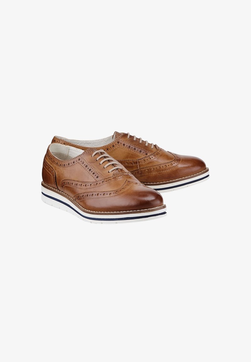 Chaussures brogue en cuir marron clair avec des détails perforés, fermeture à lacets blanche et semelles en caoutchouc blanches avec une bande noire.