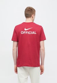 Červené bavlnené tričko s okrúhlym výstrihom, s bielym logom Nike a nápisom "OFFICIAL" potlačeným na zadnej strane. Krátke rukávy, voľný strih.