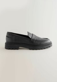 Mocasines de cuero negro con una superficie texturada, una tira ancha en el empeine y una suela de goma gruesa con surcos pronunciados.