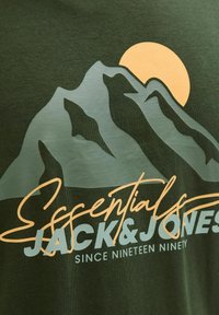 Olivenfarbenes T-Shirt mit einem Berg-Design in hellgrün und einer gelben Sonne, darunter der Schriftzug "Essentials JACK & JONES" in stilisierter Textform.