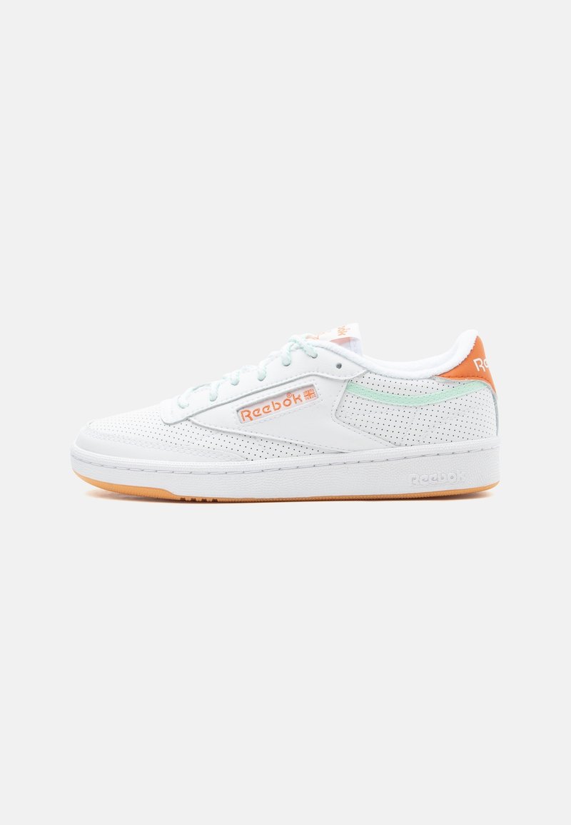 Baskets basses blanches Reebok avec un design perforé, des lacets bleu clair, des détails du logo orange et une semelle en gomme sur fond uni.