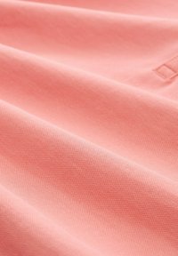 Hullámos textil felület lágy korall színben, textúrált szövésminta jellemzi. Simaság, enyhe fényesség és finom esés jellemzi.
